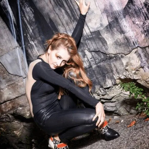 A jazz dancer crouching on rocks in a black outfit