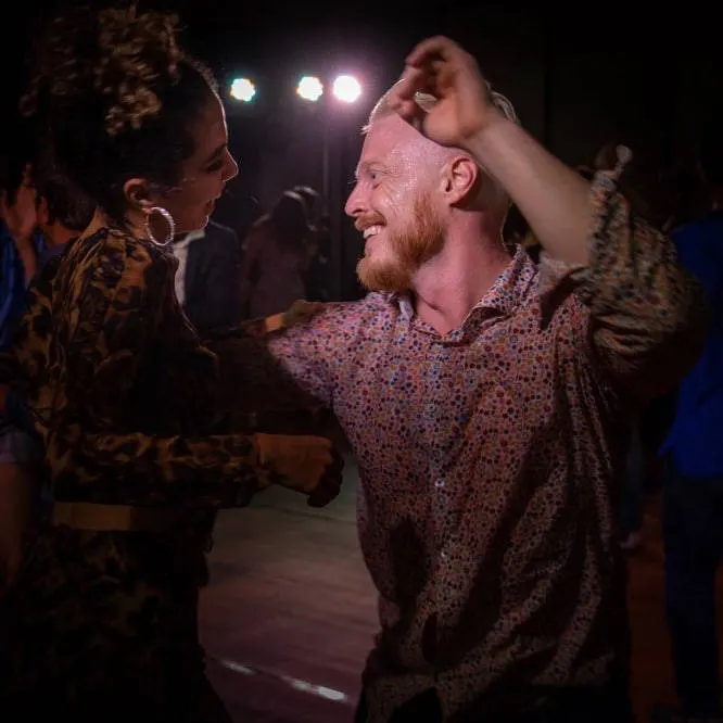 Two dancers performing reggaeton on a dark stage