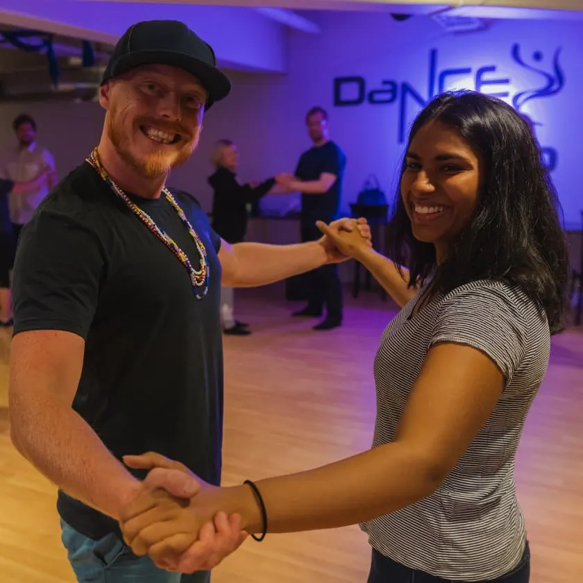 A couple laughing as they dance salsa under purple studio light